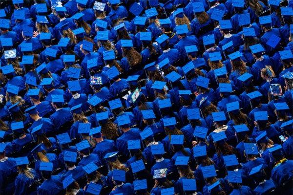 A large group of seated people wearing blue graduation caps are seen from above.