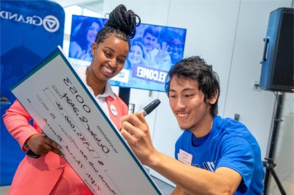  Two smiling students sign an oversized check during a check presentation event. 