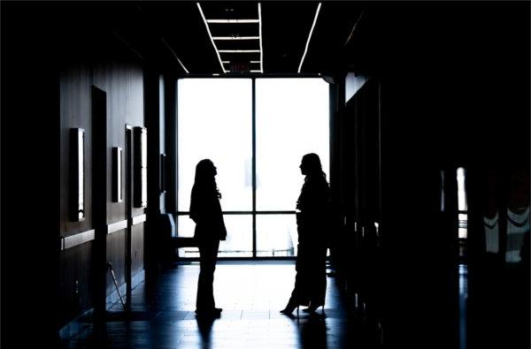  Two people are silhouetted against a window in a long hallway of an academic building. 