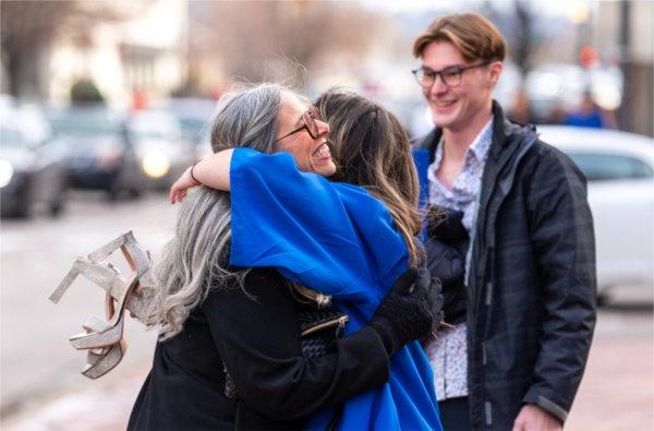  A graduate holding high heels hugs a person.